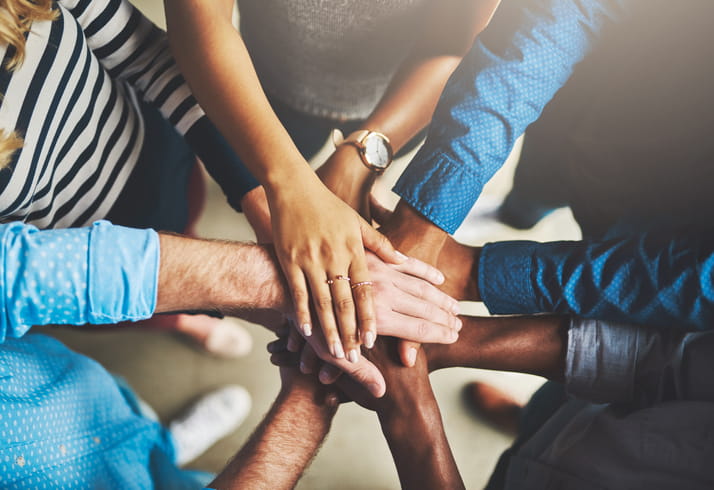The hands of five adults of multiple ethnicities stacked on top of each other in solidarity.