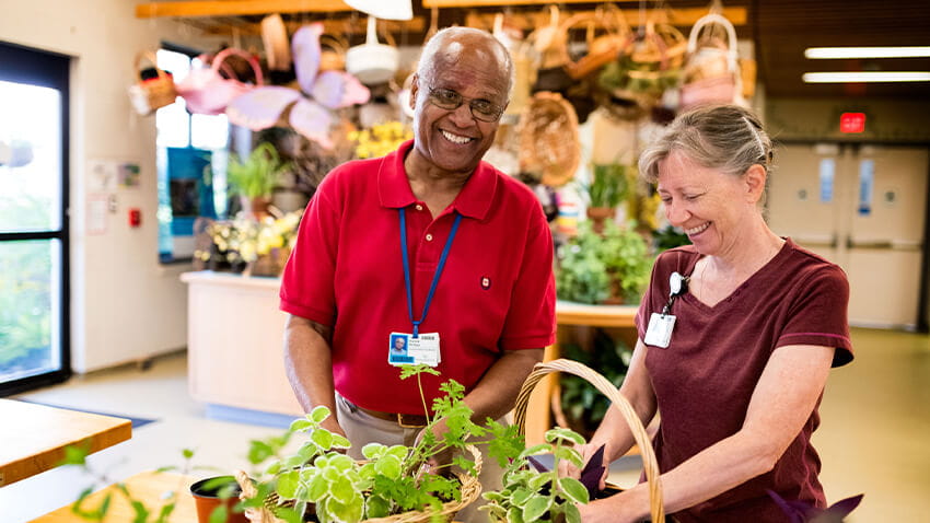 Older black man arranging plants with middle-aged white woman, both smiling