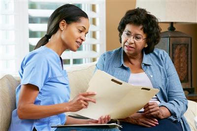 Nurse sitting with older woman going over information in file in nurse&#39;s hand