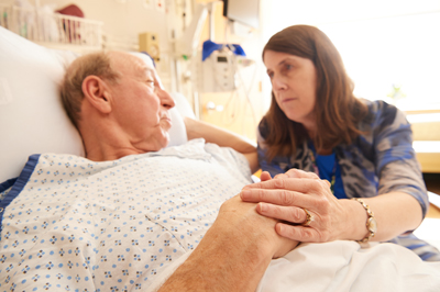 Woman at hospital bedside of man, holding hands