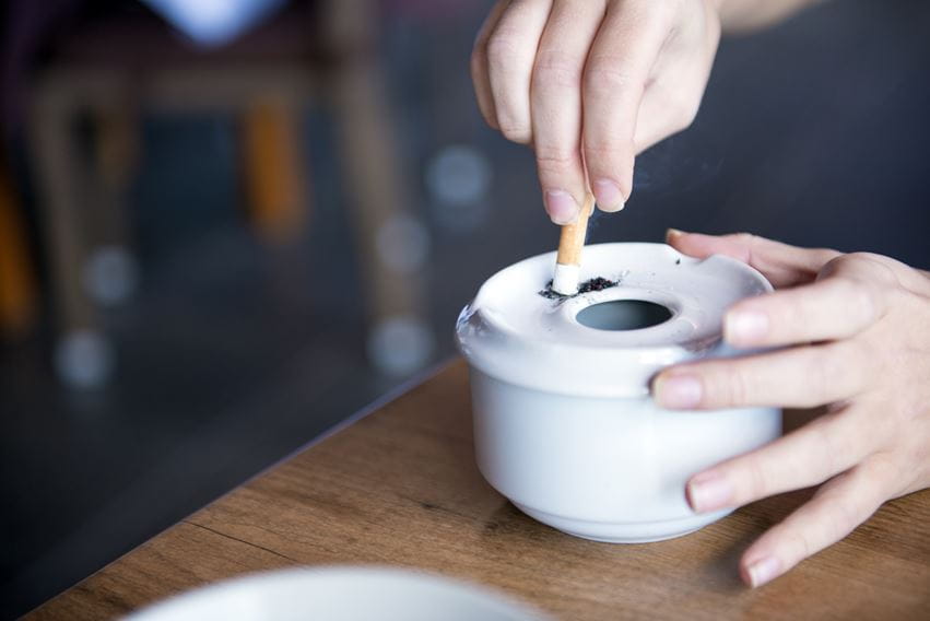 Person putting cigarette out on white ceramic ashtray