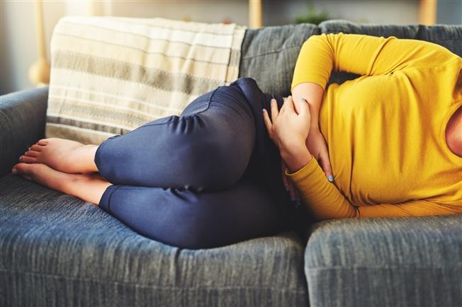 Close-up on woman laying curled up on her side on a couch with her hands wrapped over her abdomen