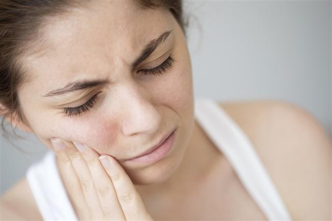 Woman placing hand on cheek with pained expression on face Woman placing hand on cheek with pained expression on face