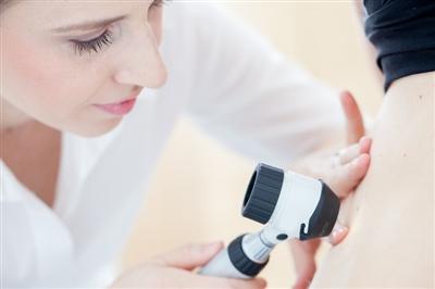 Dermatologist inspecting patient's skin with a dermascope