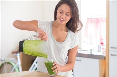 Woman pour a green smoothie into a glass from a blender
