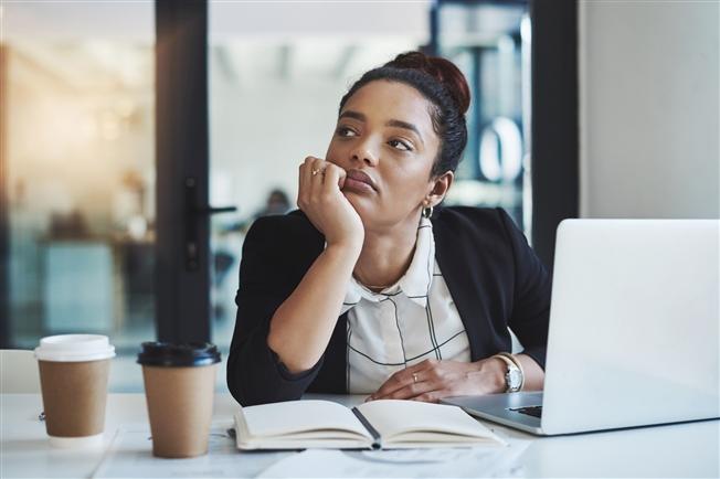 Woman sitting at desk with head propped up on her hand and looking out into the distance