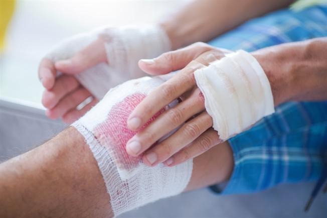 Person binding up bleeding knee with his wrapped up hands Person binding up bleeding knee with his wrapped up hands