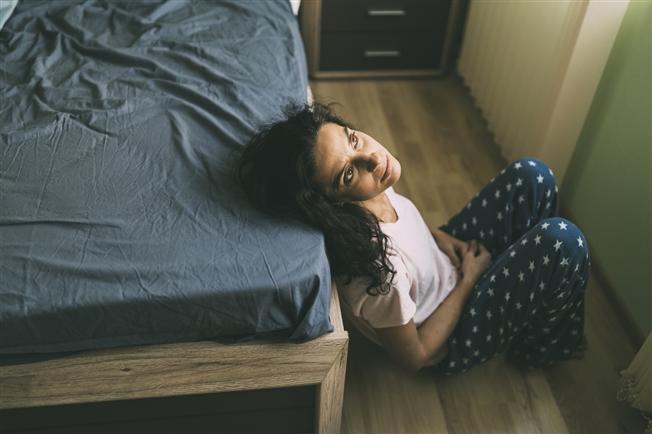 Sad looking woman sitting on floor with head leaning back on bed, looking up