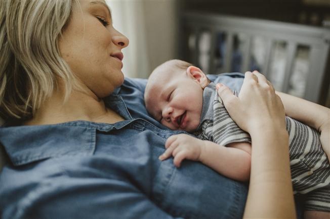 Mother reclining on rocker with baby resting on her chest