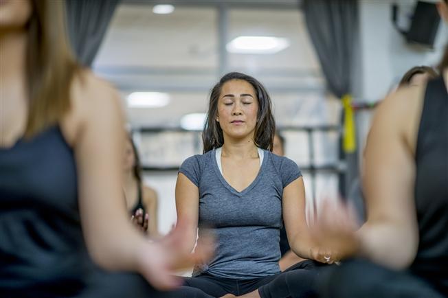 Woman sitting in a mindful meditation pose with foreground people around her out of focus Woman sitting in a mindful meditation pose with foreground people around her out of focus
