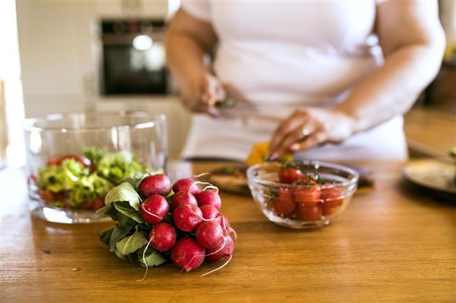 Close up on the counter filled with bowls of vegetables with a person cutting one of the items