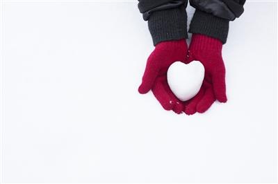 Close-up of glove-covered hands cupping a heart-shaped snow ball outside