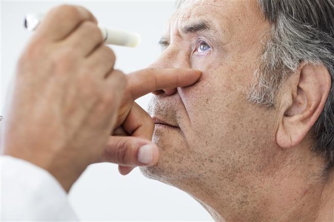Close up of doctor looking at older gentleman&#39;s eye with pen light