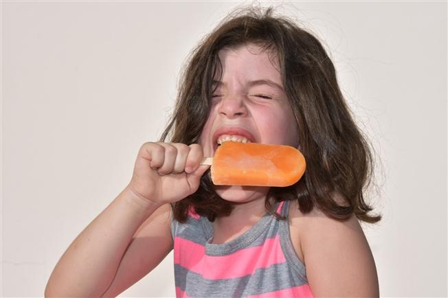 Child getting a brain freeze while biting and orange creamsicle Popsicle