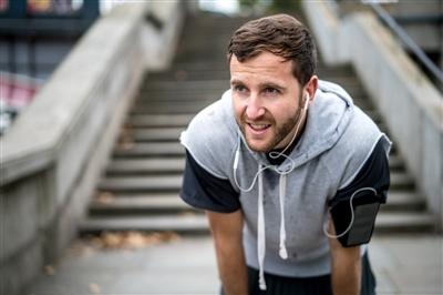 Man bent with hands resting on knees, catching a breath while working out outside