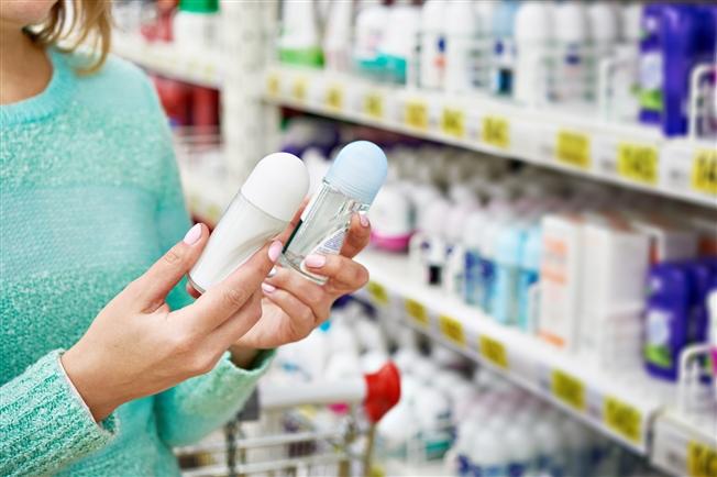 Person in grocery store aisle holding and comparing two deodorants Person in grocery store aisle holding and comparing two deodorants