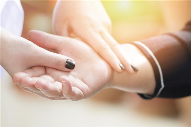 Close up of someone checking another person's pulse with two fingers on their wrist