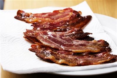 White plate with strips of bacon on top of paper towels