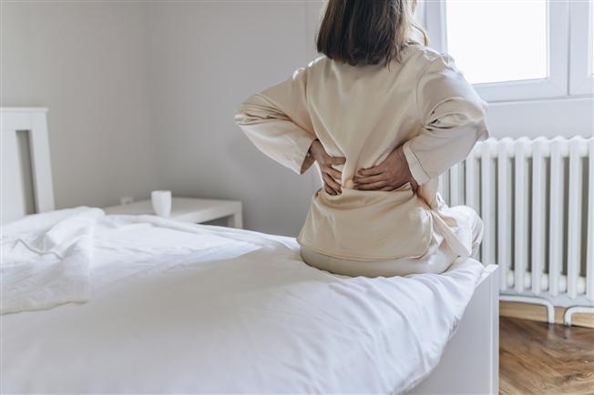 Woman sitting on edge with hands supporting lower back and stretching it out