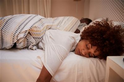 Woman sleeping on stomach on bed with arm hanging over the edge