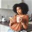 Woman leaning against kitchen counter, holding coffee cup and looking at smart phone
