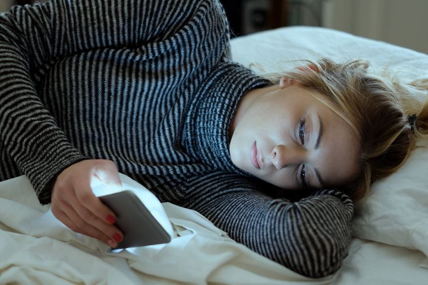 Woman looking sad scrolling phone in bed