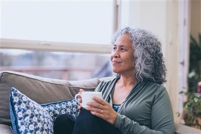Older woman holding coffee on couch looking out window