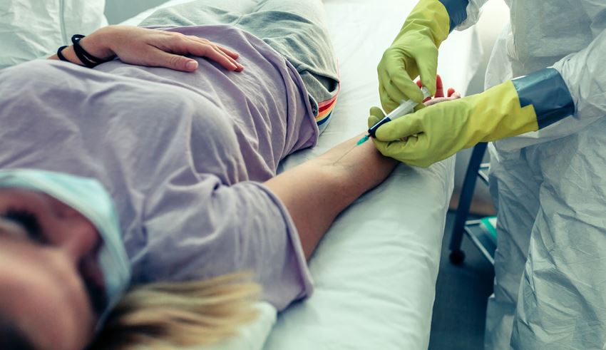 Phlebotomist drawing blood from arm of masked patient at a blood drive