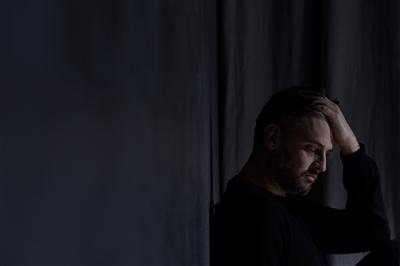 Man holding his head alone in a dimly lit room feeling isolated