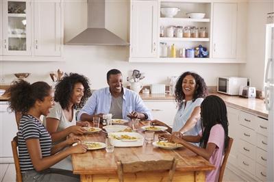 Family with teenage children eating meal around kitchen table laughing