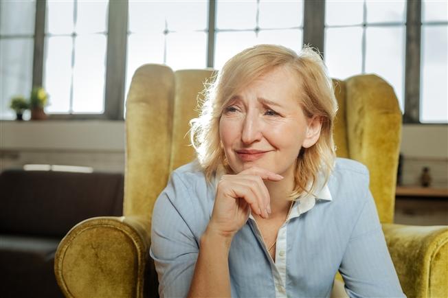 Female therapist sitting in armchair leaning forward with hand under chin with look of intense scrutiny on her face