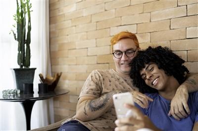 Young gay couple on couch at home looking at cell phone