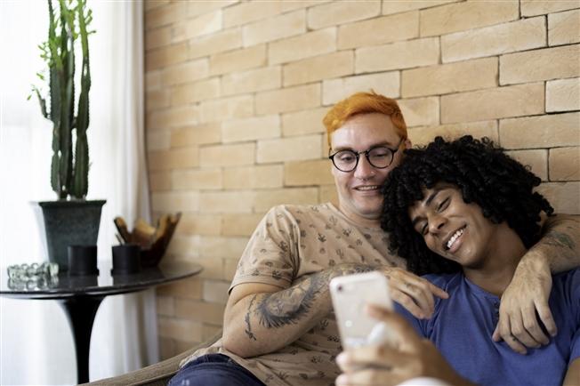 Young gay couple on couch at home looking at cell phone Young gay couple on couch at home looking at cell phone