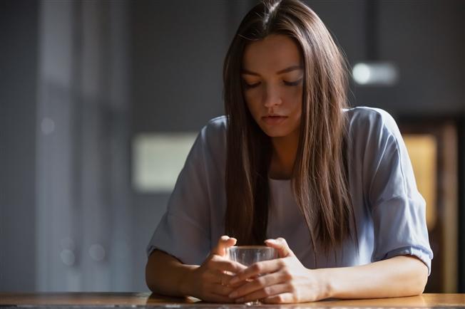 Young woman looking sad sitting alone at bar with glass of alcohol in her hand