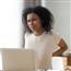 Young woman wincing at back pain from sitting at kitchen table and working
