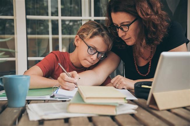 Middle aged woman at home in front of computer helping son with schoolwork