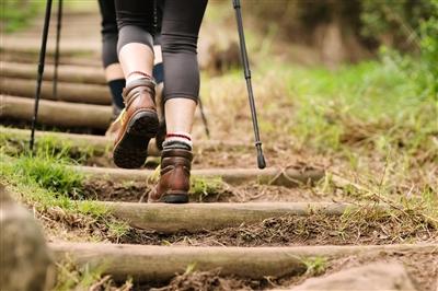 Rear view shot of a woman hiking up the steps on mountain trail using a hiking stick