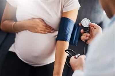Pregnant woman with hand on stomach getting blood pressure taken by clinician in a doctors office setting