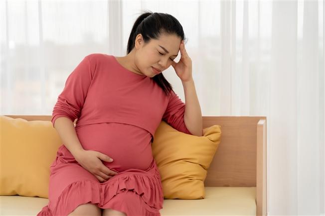 Young pregnant woman with eyes closed clutching head in pain and cradling stomach Young pregnant woman with eyes closed clutching head in pain and cradling stomach