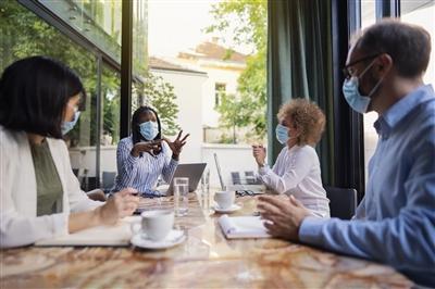 Diverse group of business people having a meeting at the coffee shop while wearing protective masks during coronavirus pandemic