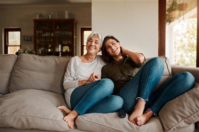 Senior mother and younger daughter on couch smiling with arms around each other