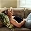 Young woman laying on couch grimacing in pain with hand to stomach