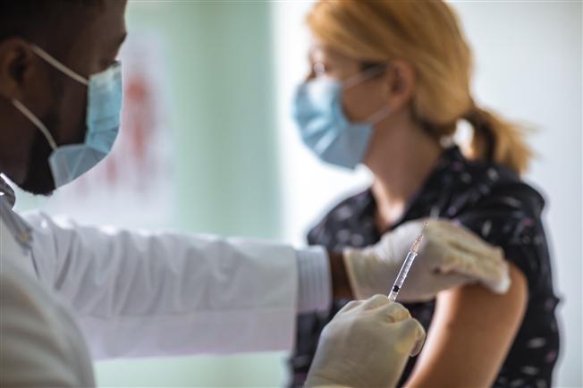 Woman wearing a mask is getting a flu vaccination administered by doctor in a mask