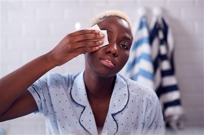 Young woman removing eye makeup in bathroom mirror