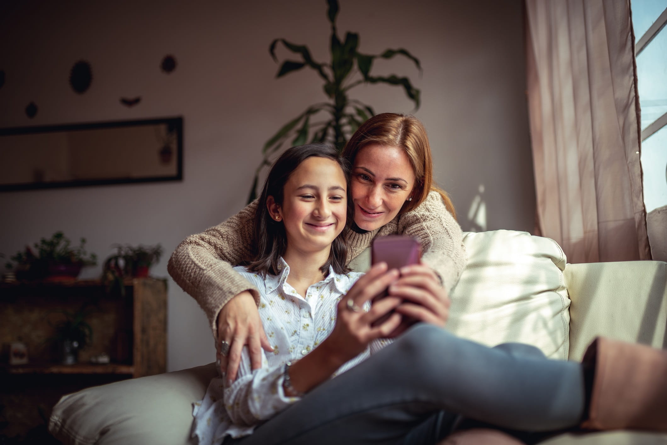 Teenage girl using a smartphone and smiling as mom gives her a hug