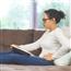 Young woman on couch wincing as she touches hand to lower belly