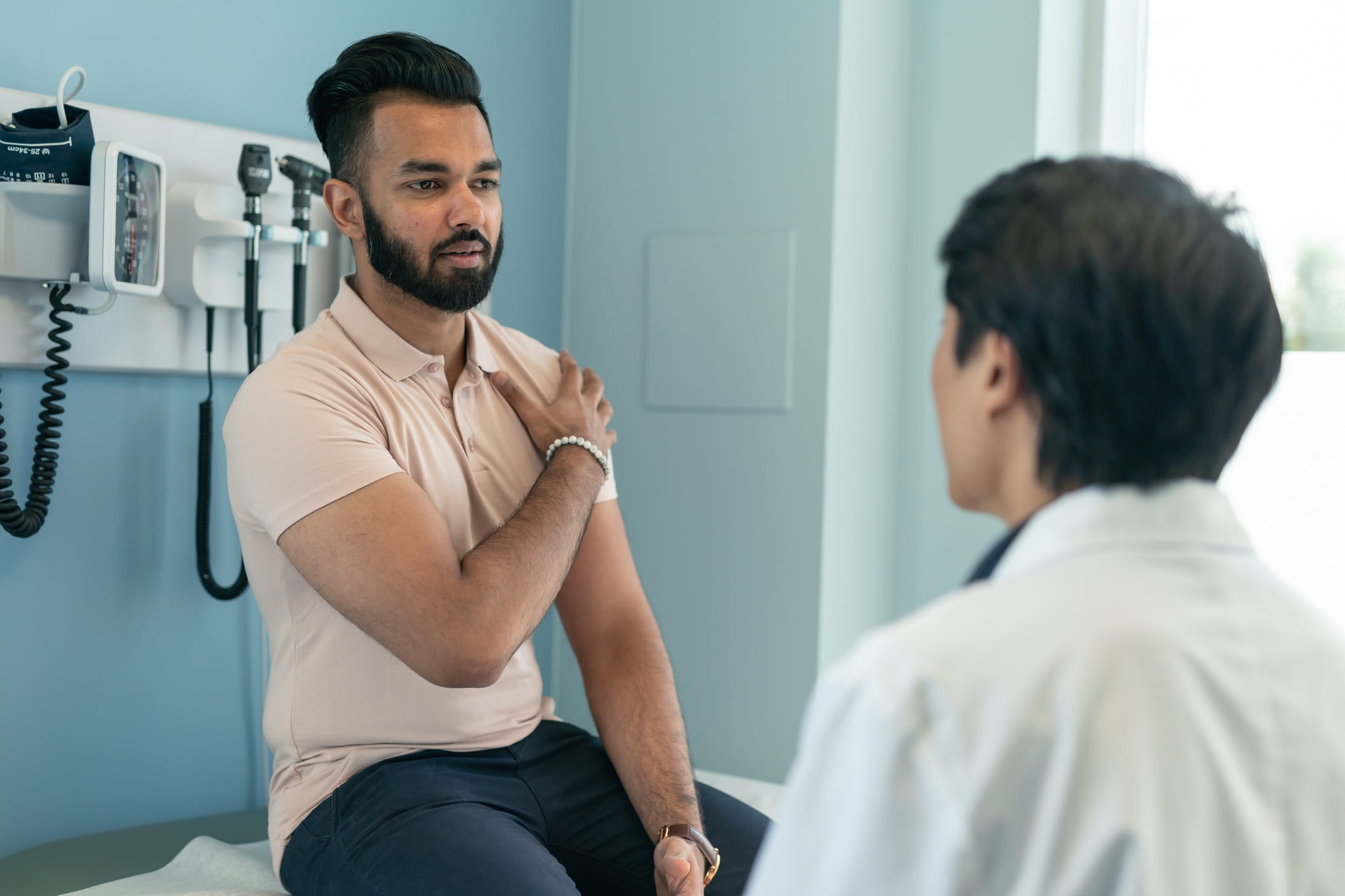 Young man at doctors office demonstrating pain in shoulder