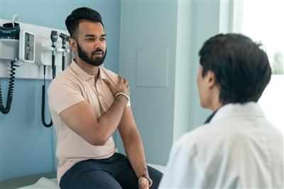Young man at doctors office demonstrating pain in shoulder