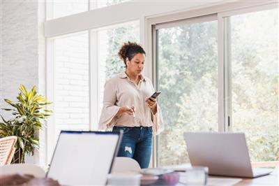 Businesswoman working at home standing and holding cell phone