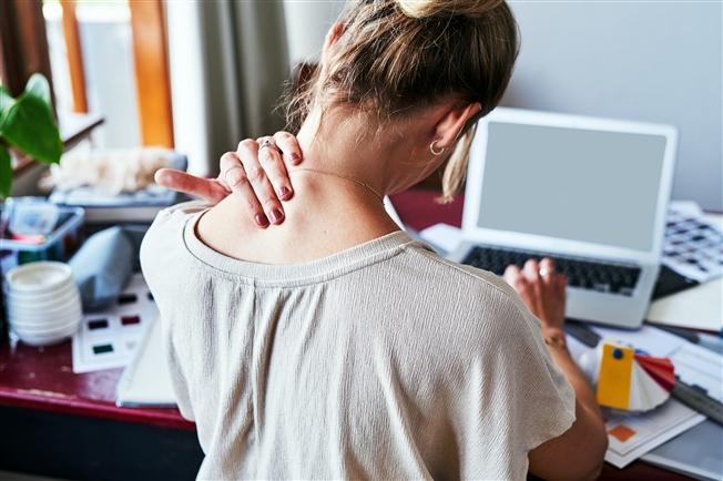 Rearview shot of a woman experiencing discomfort in her shoulders while sitting at her desk Rearview shot of a woman experiencing discomfort in her shoulders while sitting at her desk